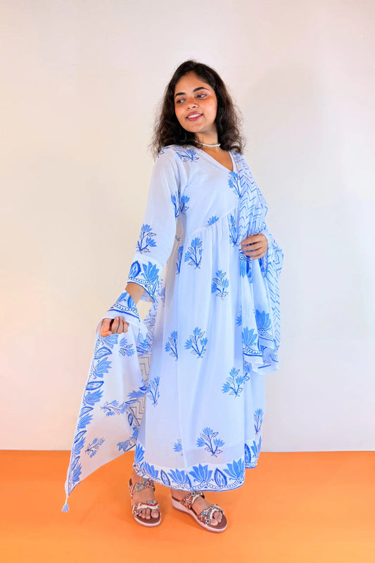 A woman modeling a light blue and white floral print kaftan dress with matching dupatta, standing against a plain beige wall and orange floor.