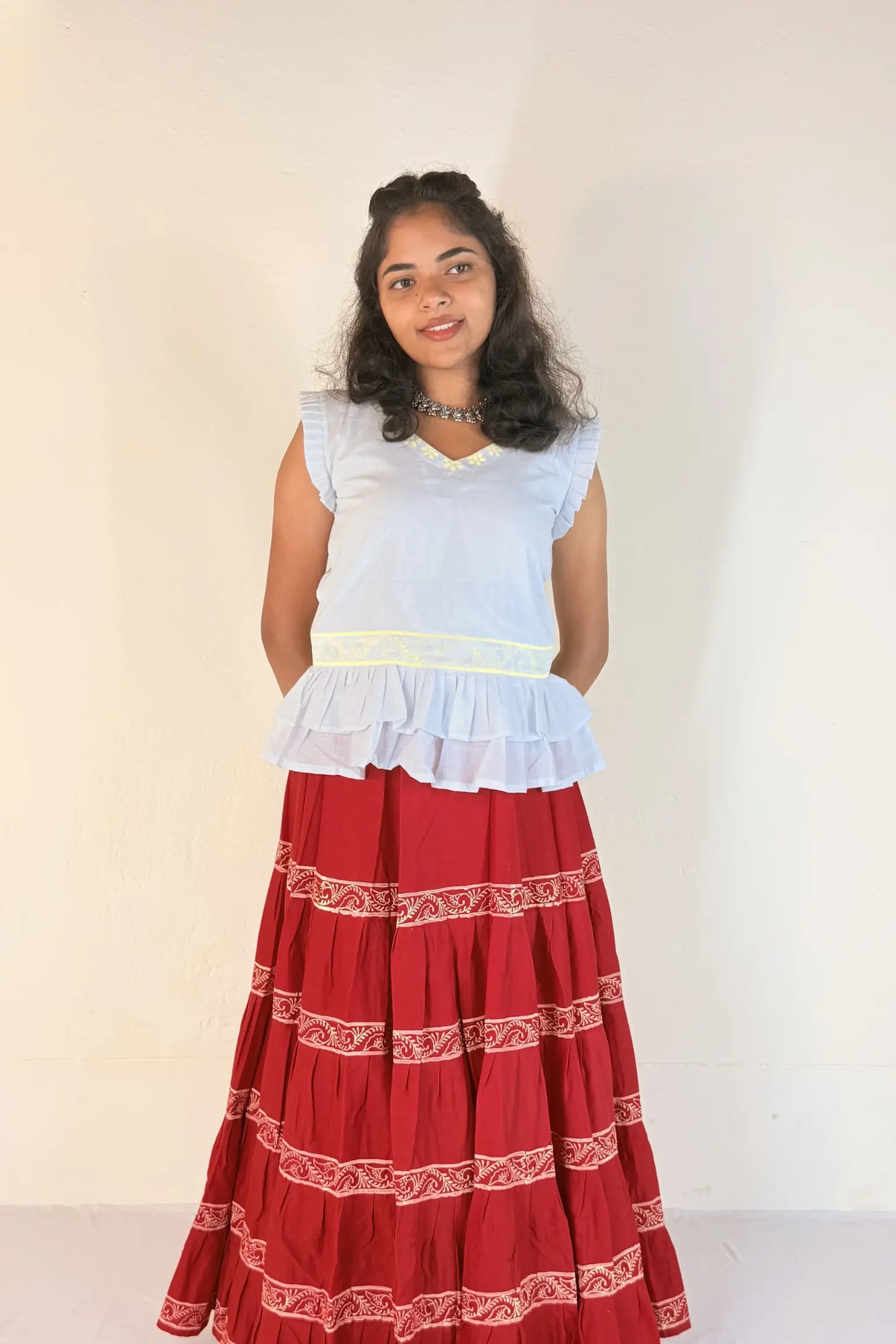 Woman wearing a white top and red skirt with white patterns on a plain background