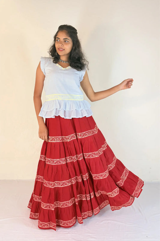 A woman wearing a white sleeveless top and red skirt with white patterns on a white background