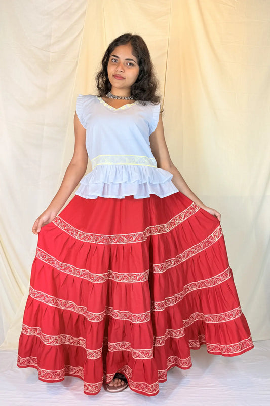 Woman wearing a white top and red skirt with white embroidery against a plain background