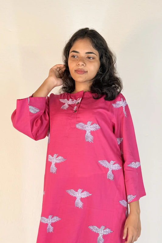 Woman wearing a pink traditional outfit with white patterns on a plain background