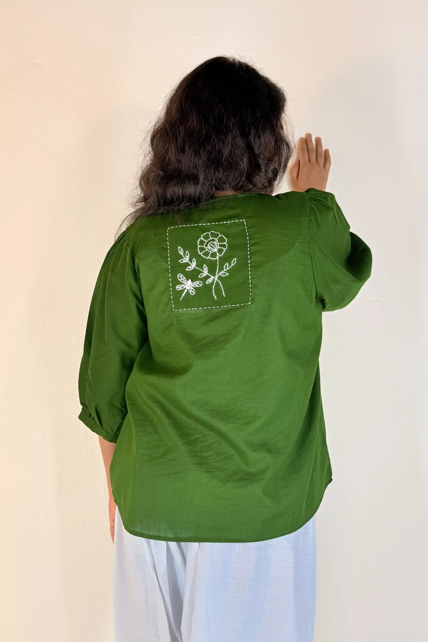 Person wearing a green shirt with a floral design on the back against a plain background