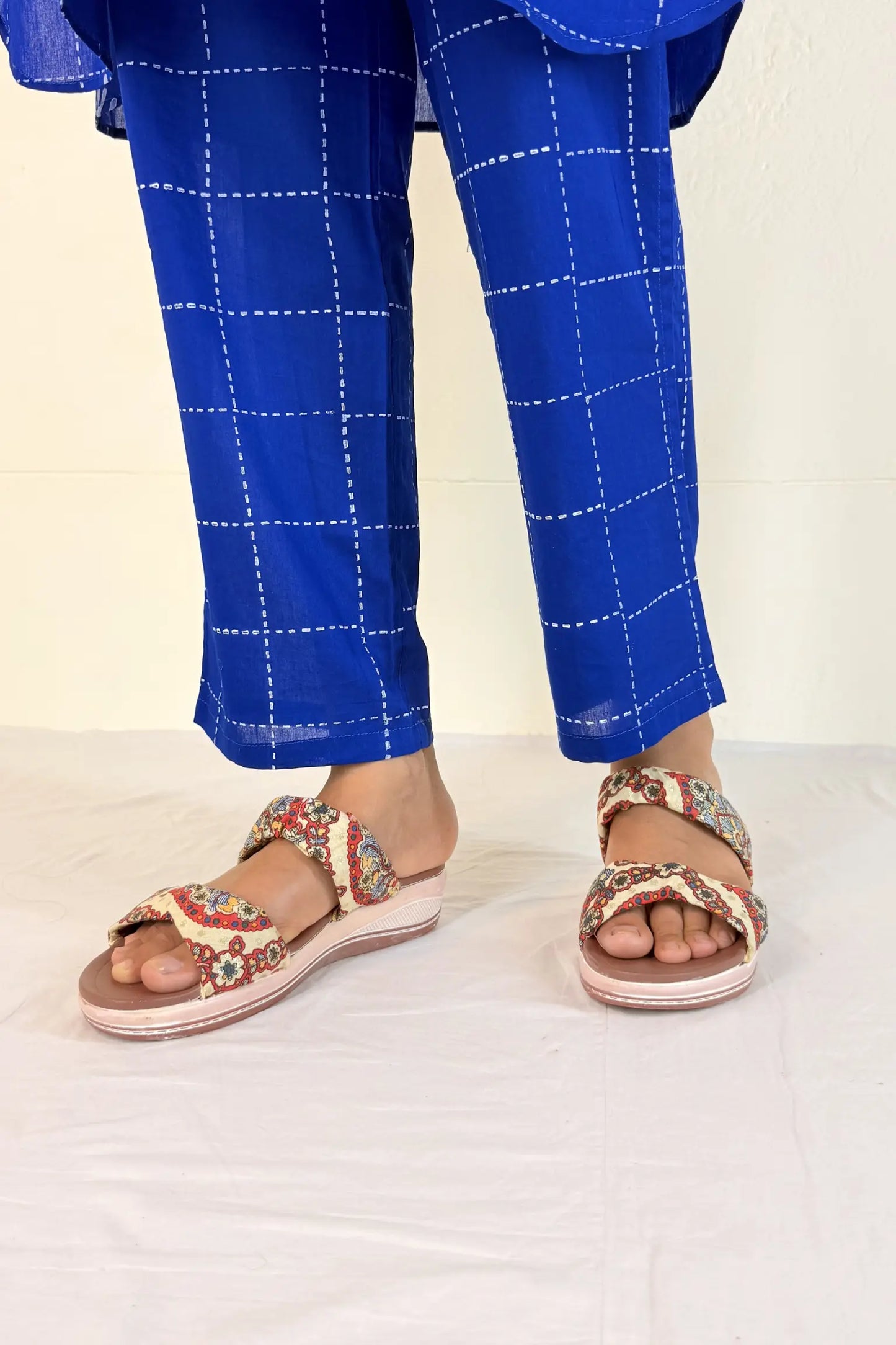 Person wearing blue checkered pants and embellished sandals on a white background