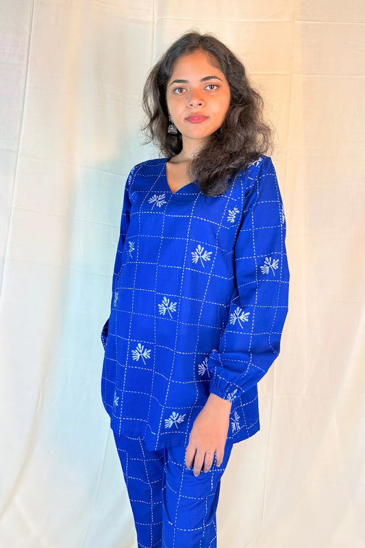 Woman wearing a blue embroidered outfit against a white curtain background