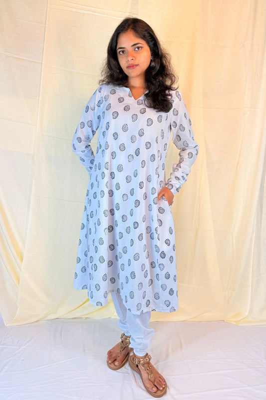 Woman wearing a light blue kurta with white pants against a beige curtain background