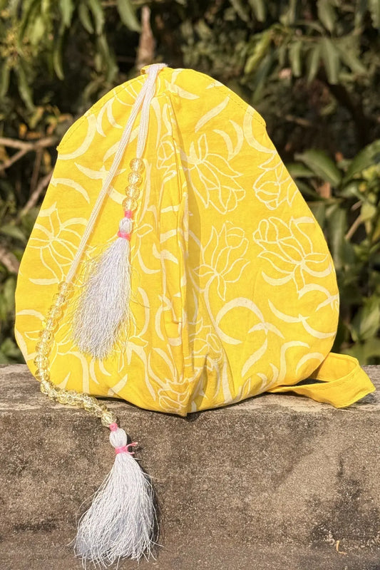 Yellow fabric pouch with floral patterns and tassels on a stone surface with green foliage in the background