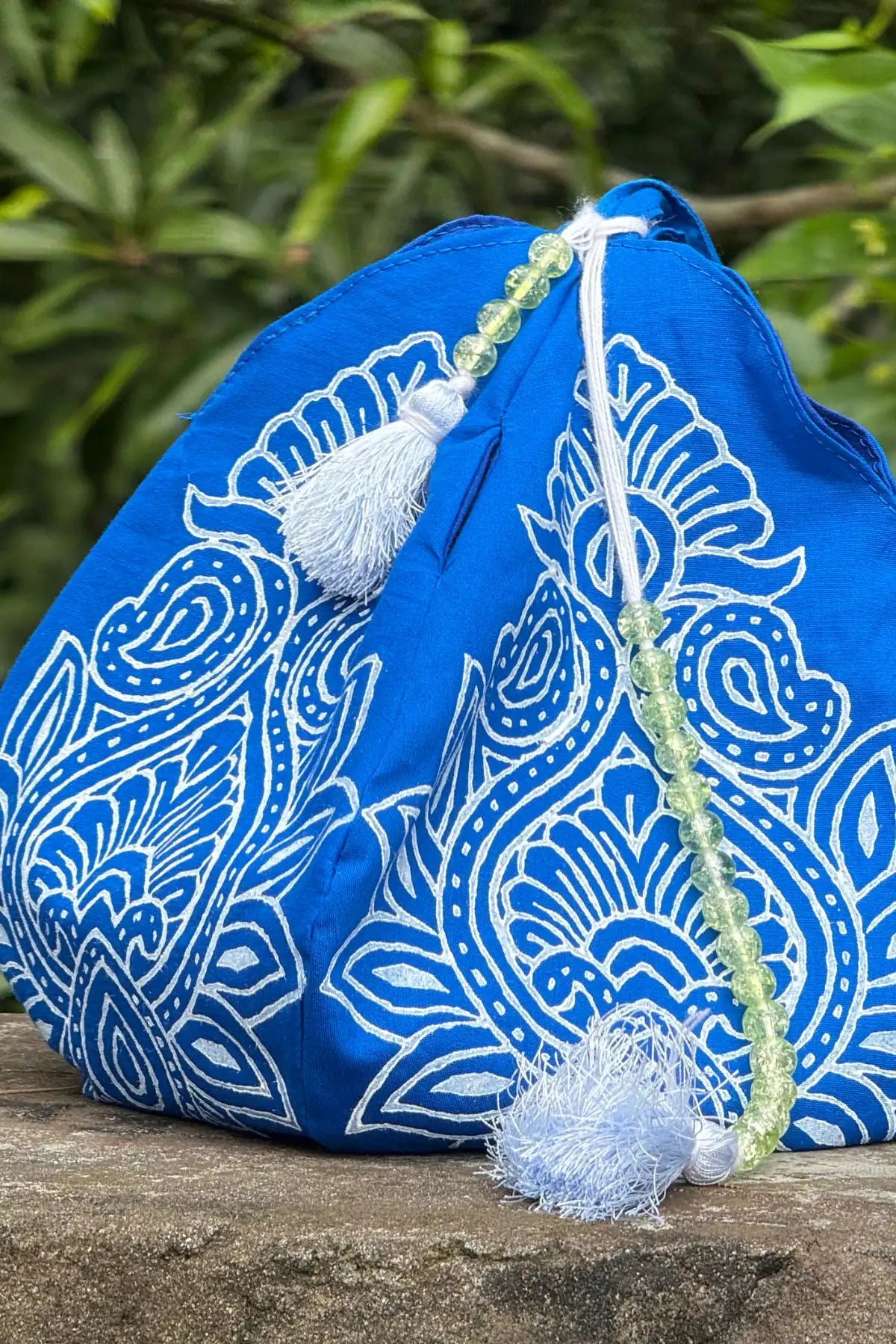 Handcrafted indigo japa mala bag with white hand block floral motif, tassel and bead detailing, photographed outdoors
