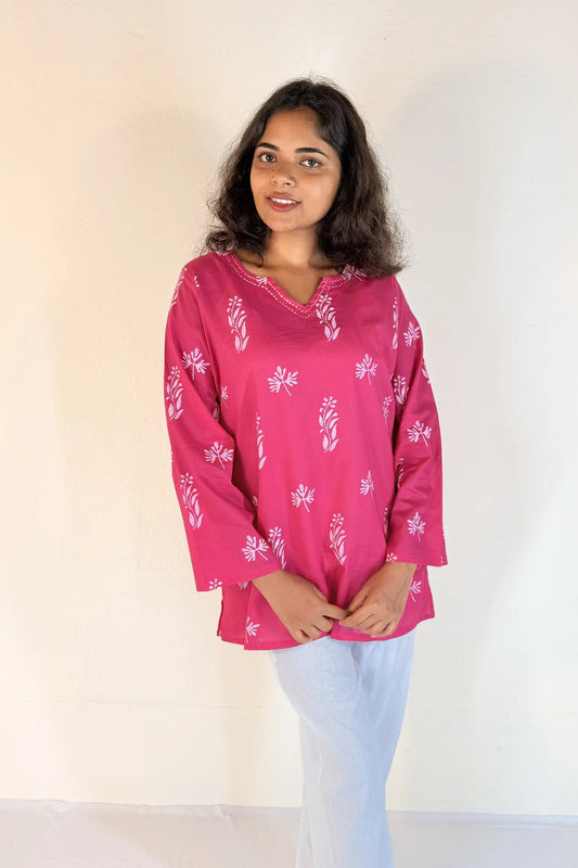 Woman wearing a pink blouse with white patterns against a plain background