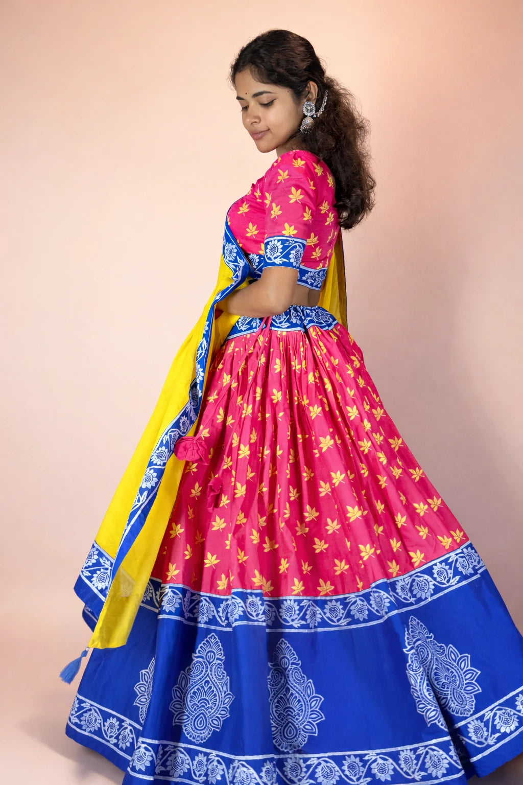 Woman wearing a vibrant pink and blue traditional outfit with yellow dupatta on a beige background