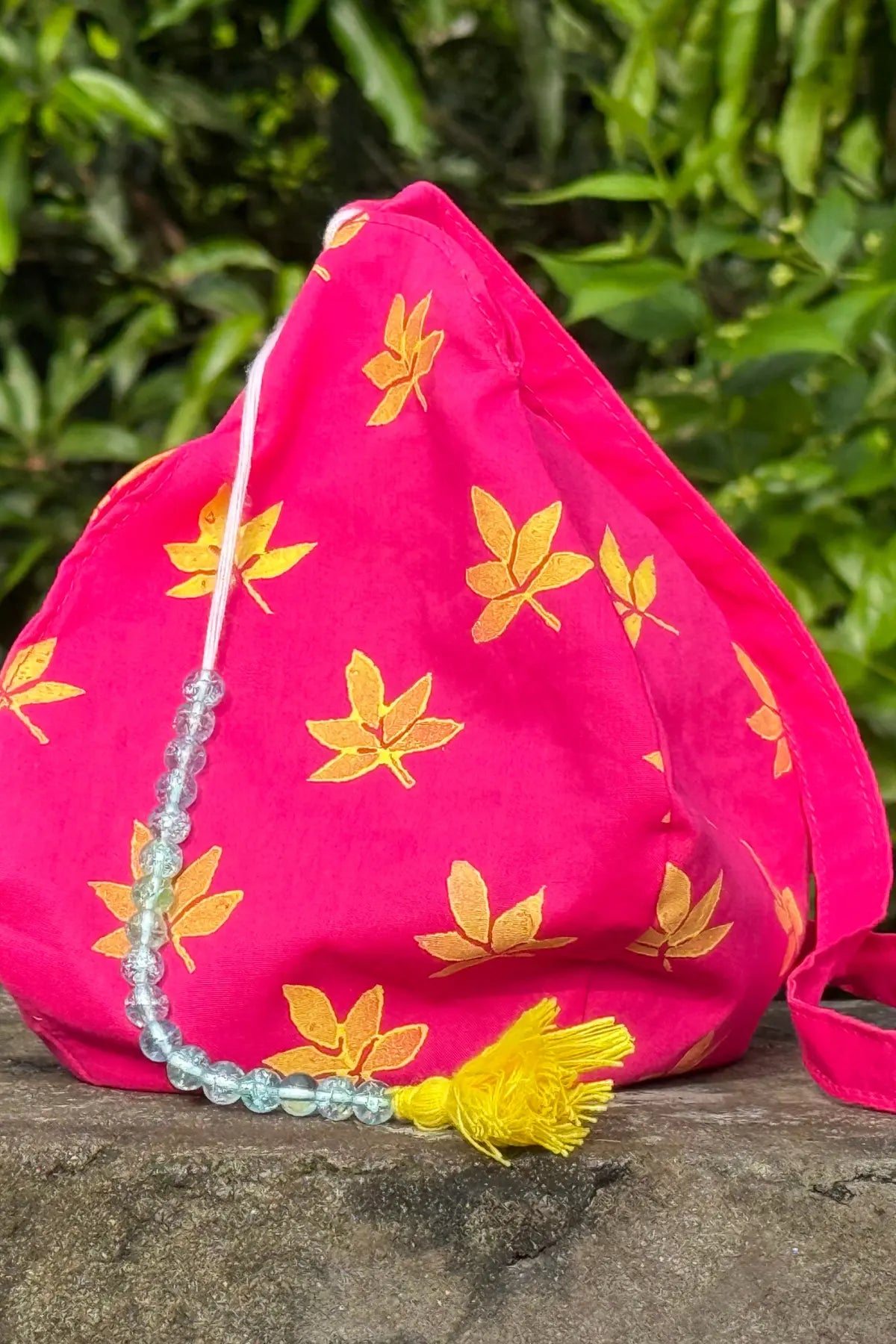 Handcrafted pink cotton japa mala bag with yellow leaf block print, bead string and tassel detail, photographed outdoors