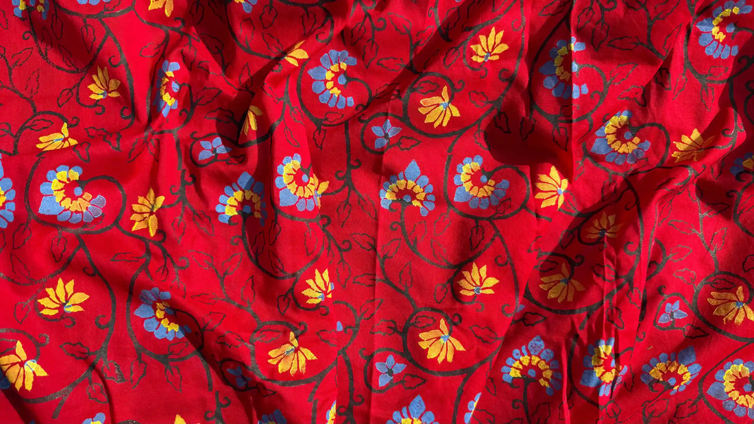 Red cotton fabric with colorful hand-printed floral motifs, showing soft natural color variations and artisan-crafted pattern details.