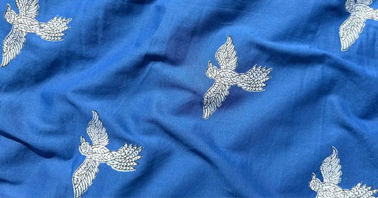 Close-up of Meghambara blue fabric featuring white flying bird motifs inspired by freedom and the open sky.