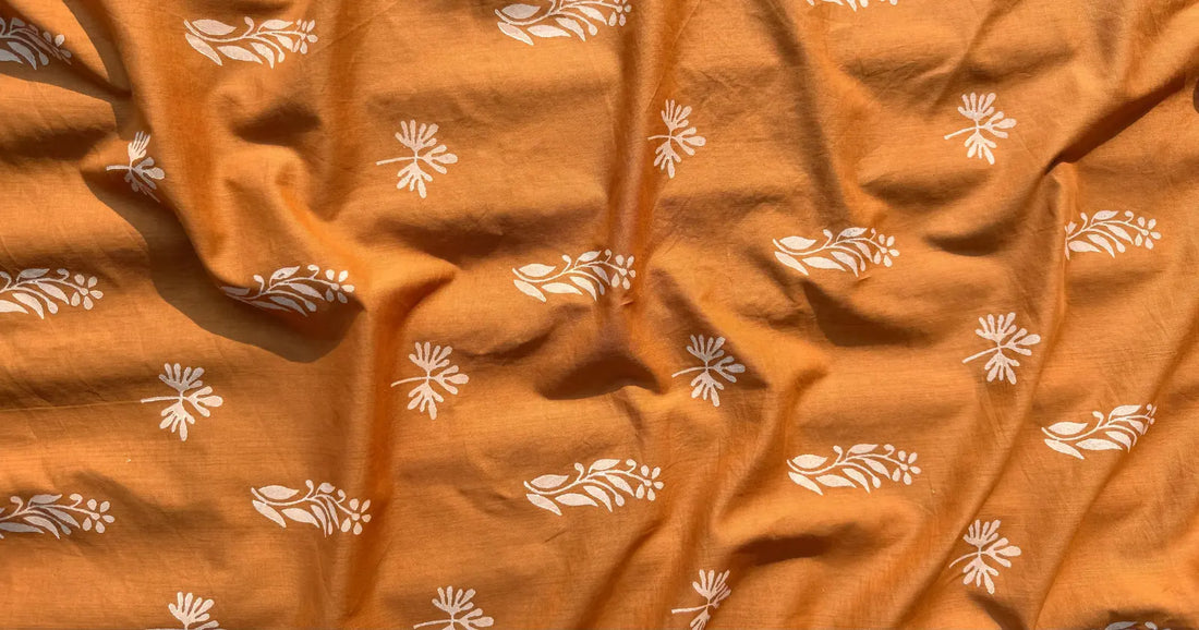 Close-up of Meghambara’s handmade block print fabric in warm terracotta orange, featuring delicate white floral motifs inspired by a tiny forgotten block.