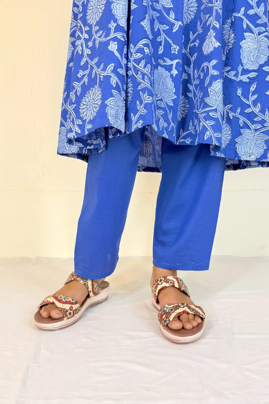 Person wearing a blue floral dress and pants with sandals on a light background