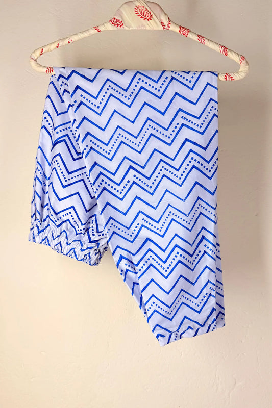 Blue and white zigzag patterned fabric draped over a cream-colored wooden hanger with red floral details, set against a plain beige wall.