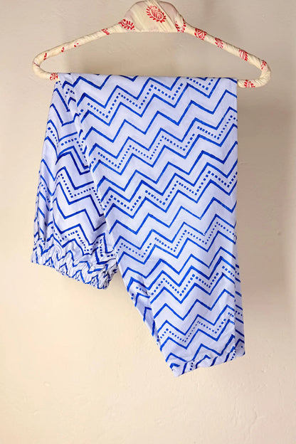 Blue and white zigzag patterned fabric draped over a cream-colored wooden hanger with red floral details, set against a plain beige wall.