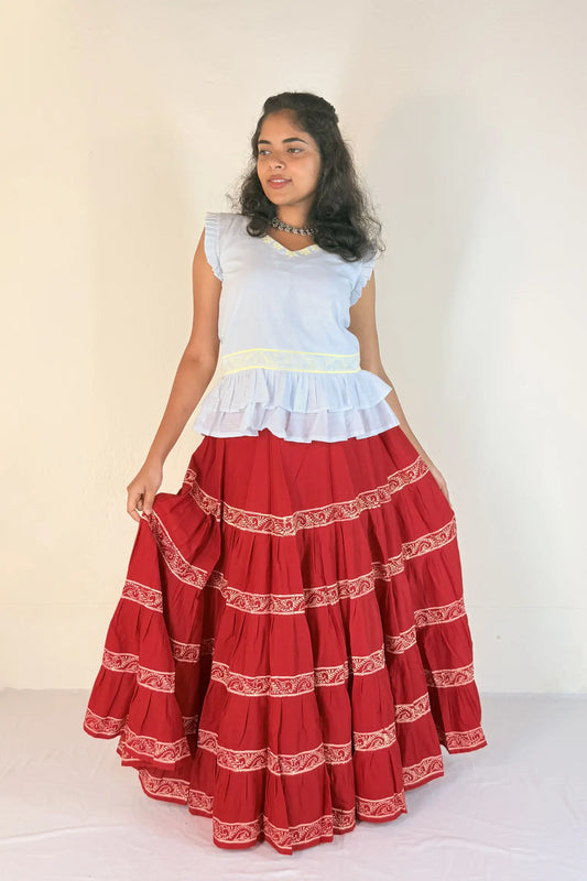Woman wearing a white top and red skirt with white patterns on a plain background
