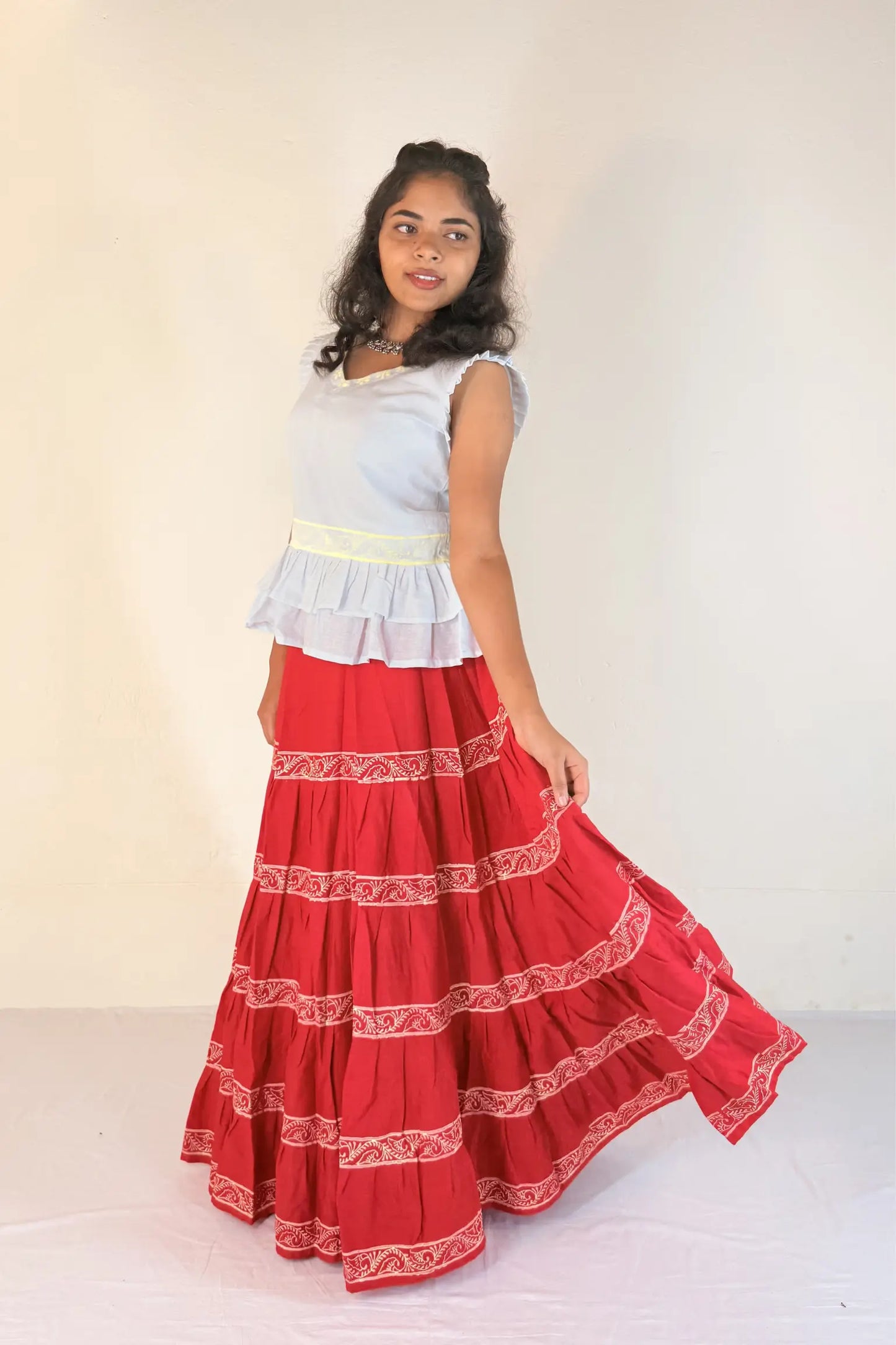 Woman wearing a white top and red skirt with white patterns on a plain background