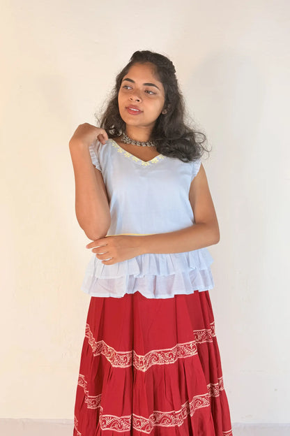 Woman wearing a white top and red skirt with white patterns on a plain background