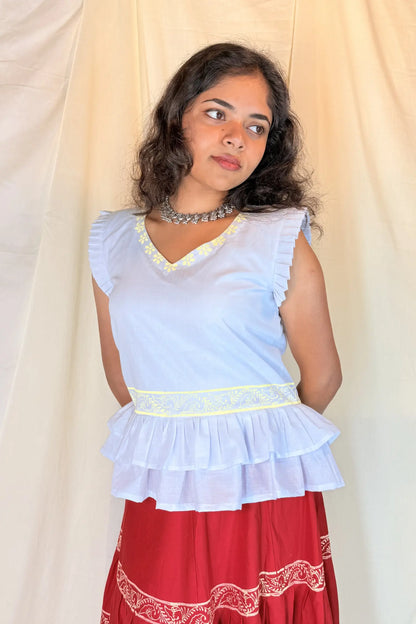 Woman wearing a white top with ruffled layers and a red skirt against a beige background