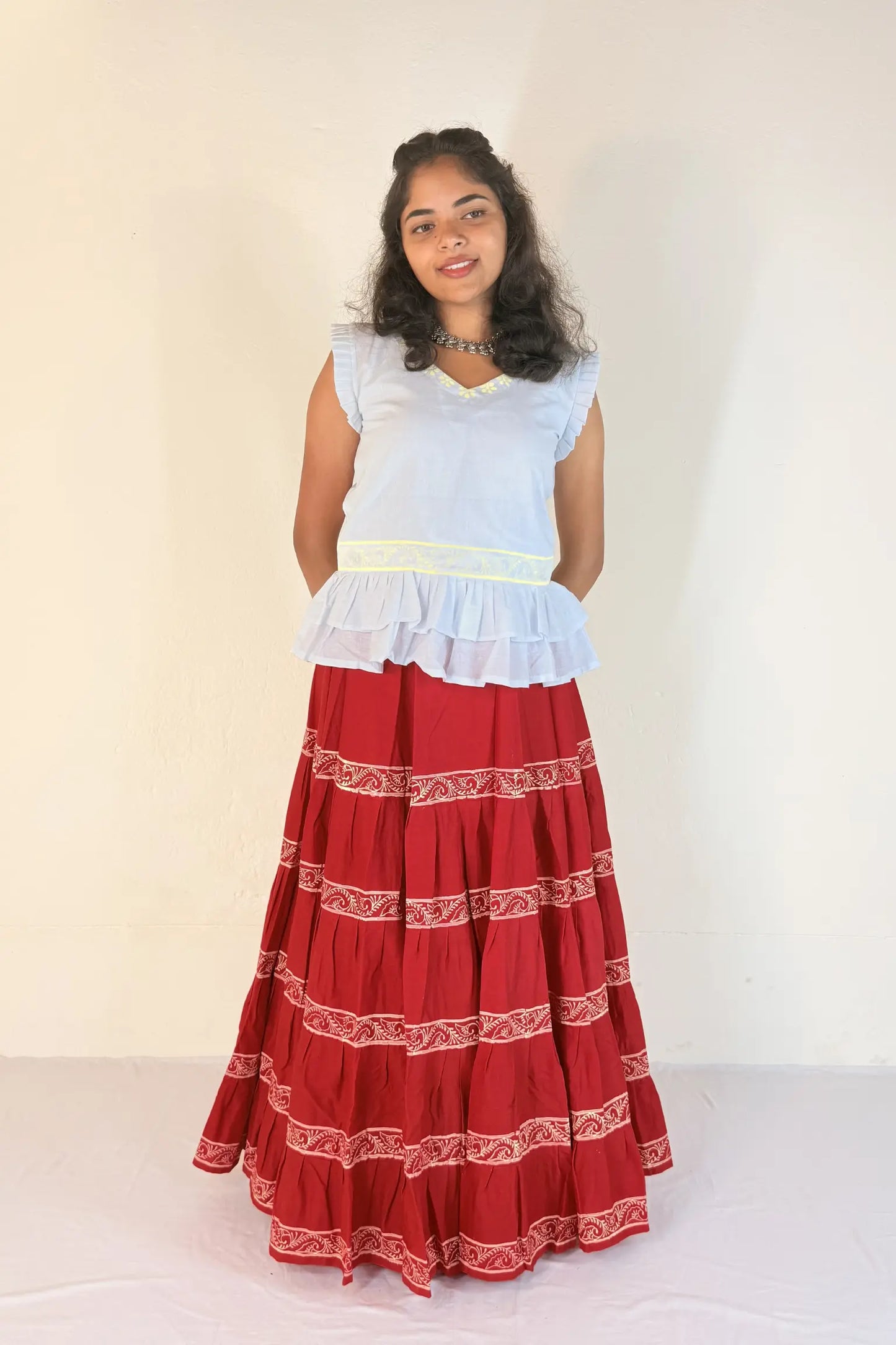 Woman wearing a white top and red skirt with white patterns on a plain background