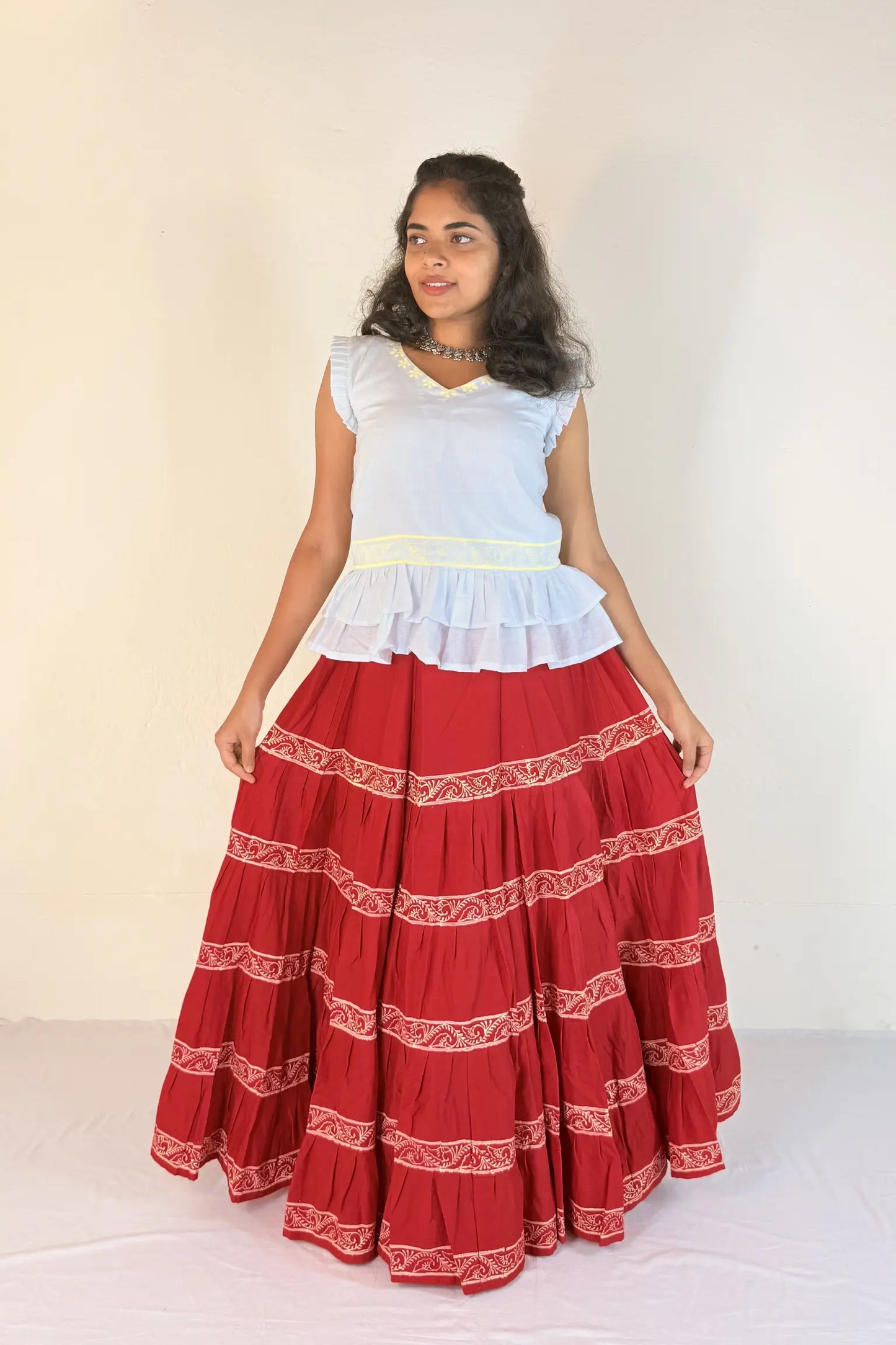 Woman wearing a white top and red skirt with white patterns on a plain background