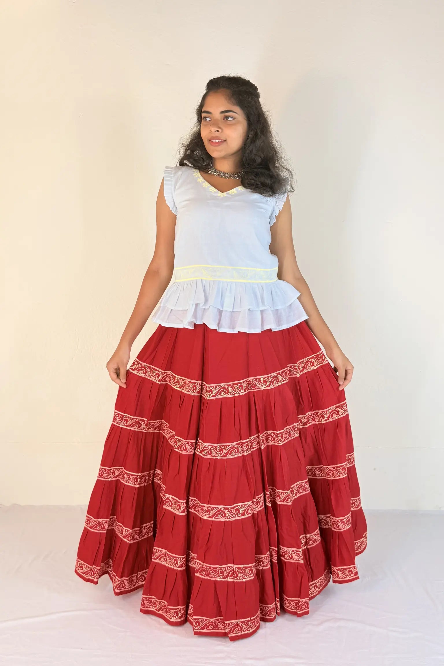 Woman wearing a white top and red skirt with white patterns on a plain background