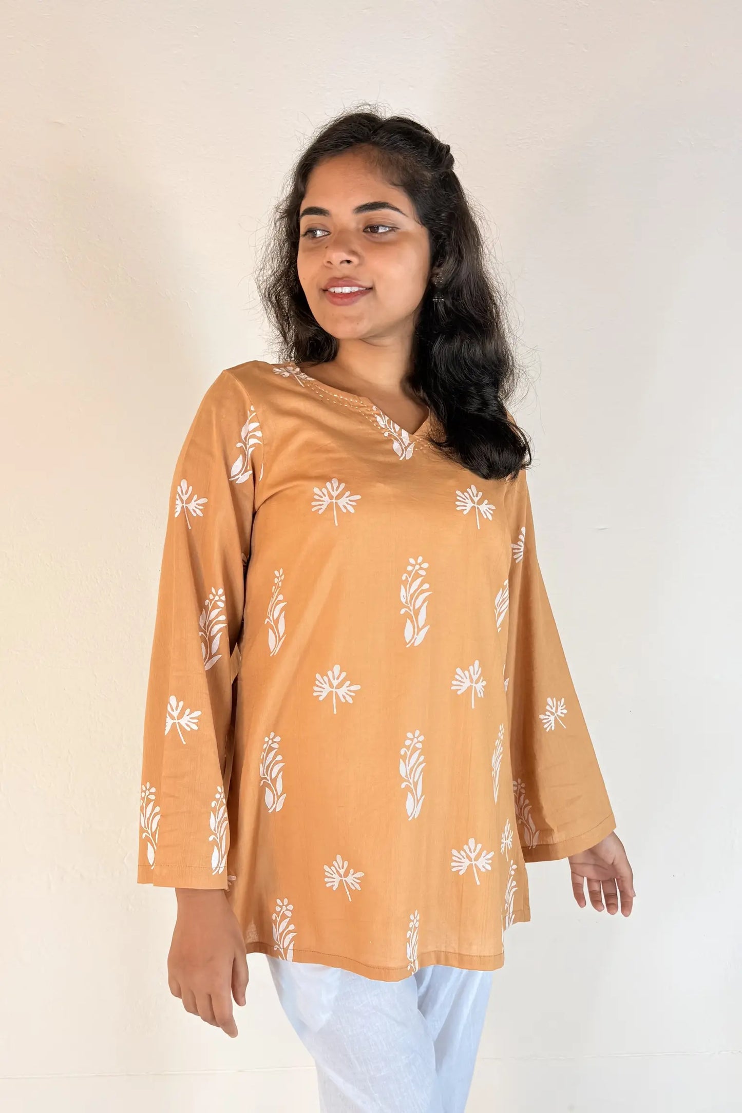 Woman wearing a mustard yellow blouse with white floral patterns on a plain background