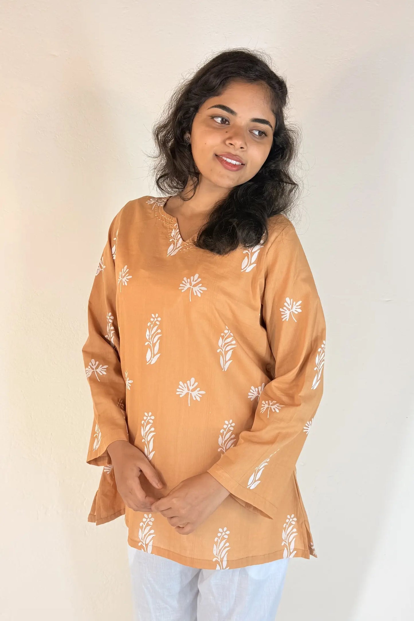 Woman wearing a mustard yellow top with white floral patterns on a plain background