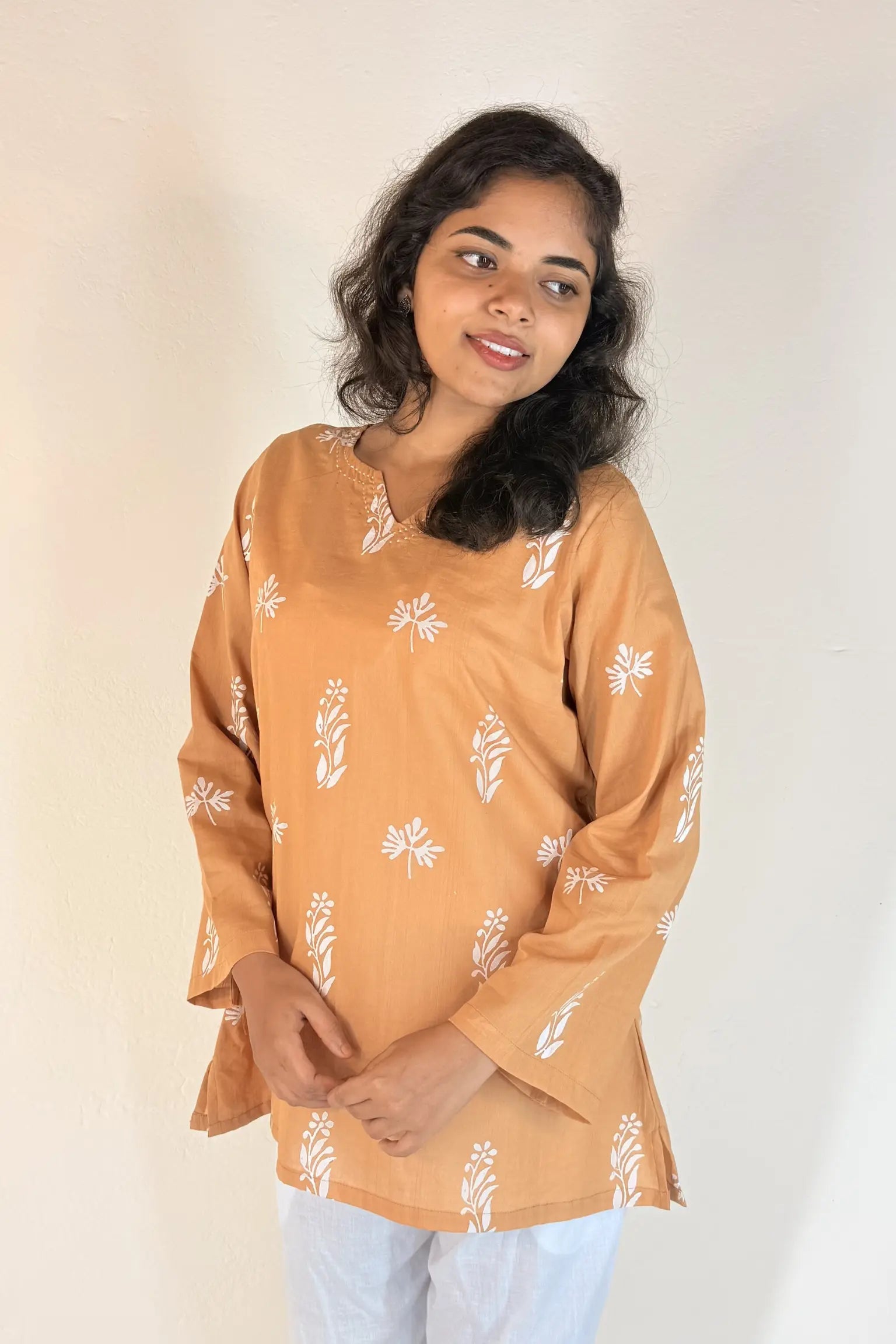 Woman wearing a mustard yellow top with white floral patterns on a plain background