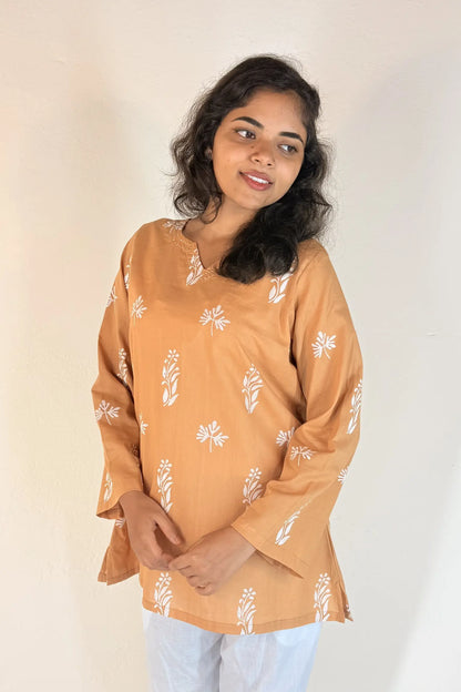 Woman wearing a mustard yellow top with white floral patterns on a plain background
