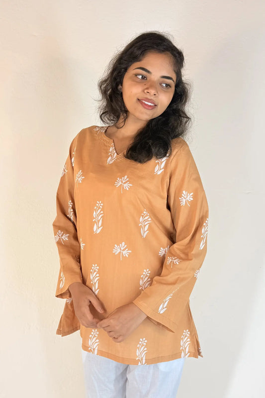 Woman wearing a mustard yellow top with white floral patterns on a plain background