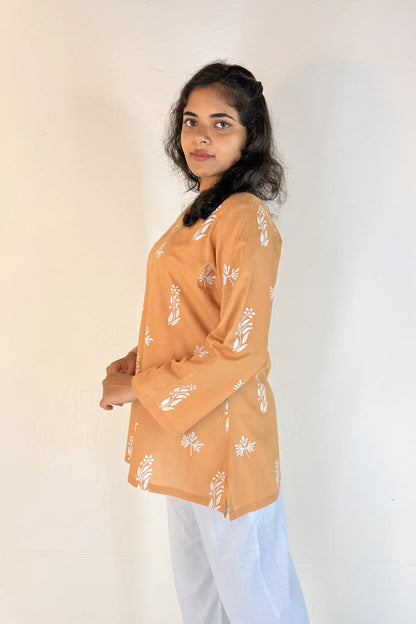 Woman wearing a mustard yellow floral blouse against a white background