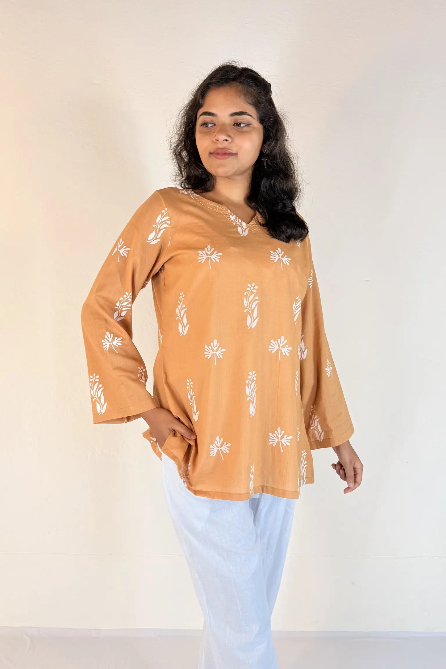 Woman wearing a brown floral top and light blue pants against a white background