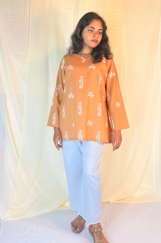 Woman wearing an orange floral blouse and white pants against a plain background