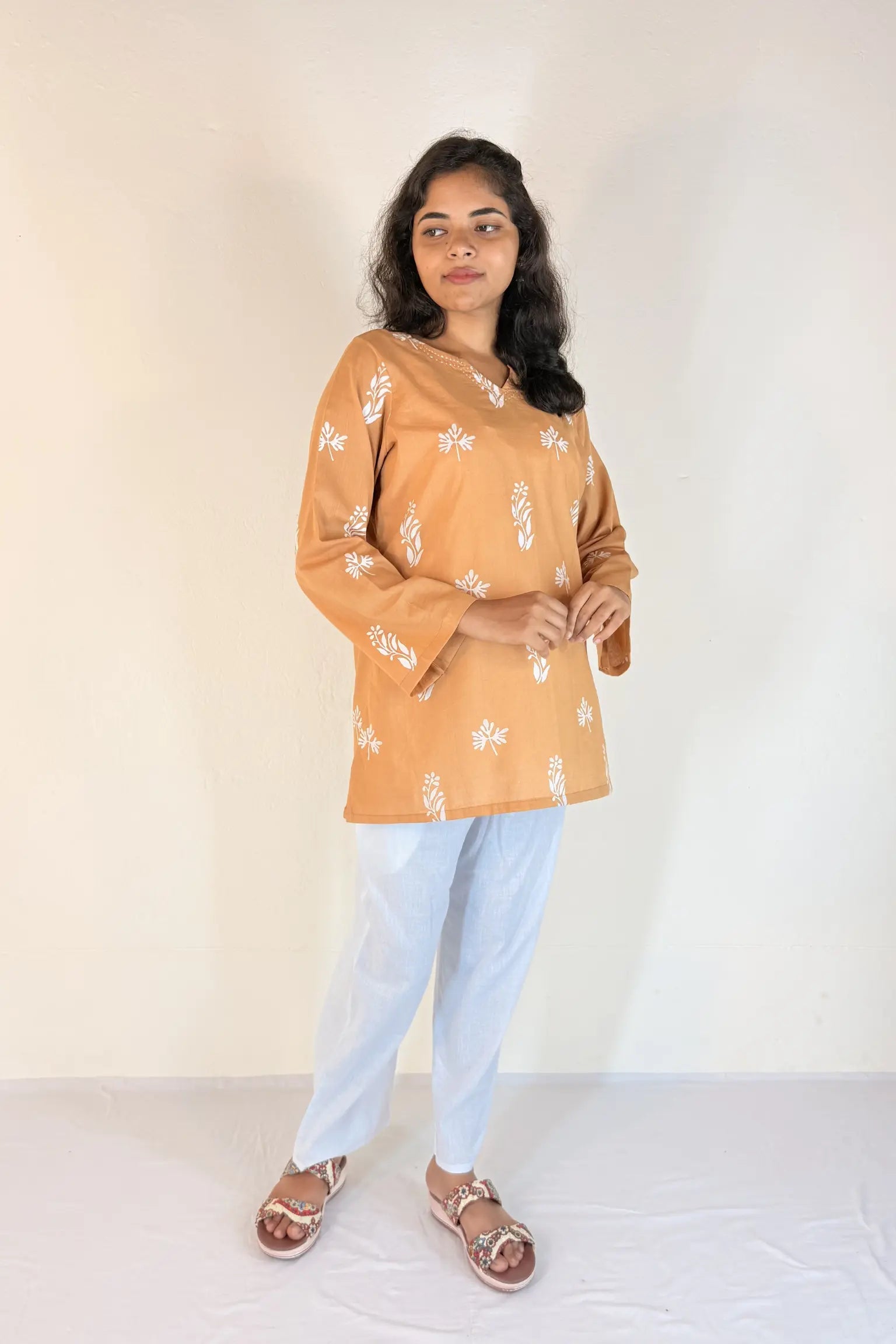 Woman wearing a mustard yellow floral top and light blue pants against a white background