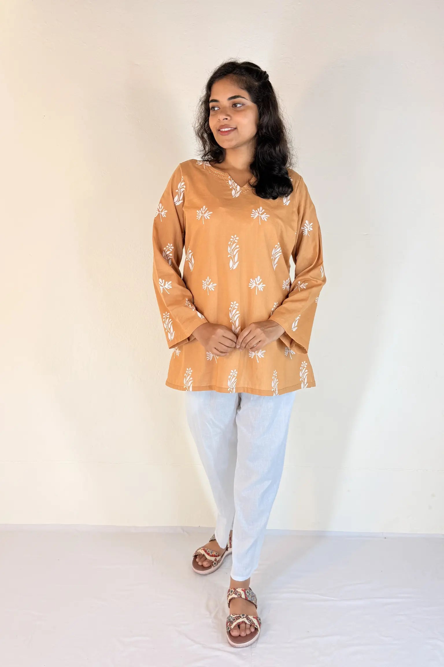 Woman wearing a mustard yellow floral top and light blue jeans against a white background