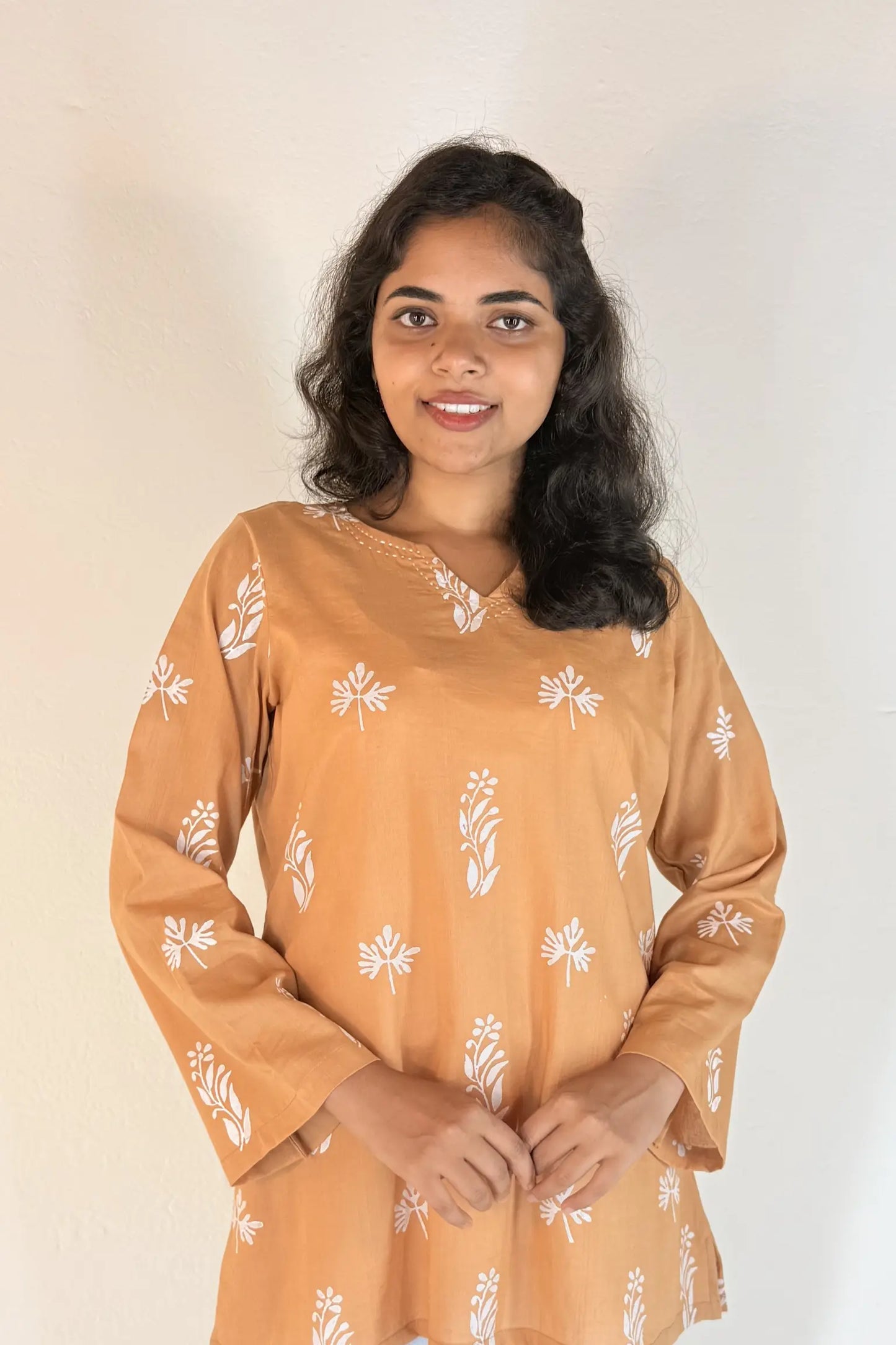Woman wearing a brown dress with white floral patterns against a plain background