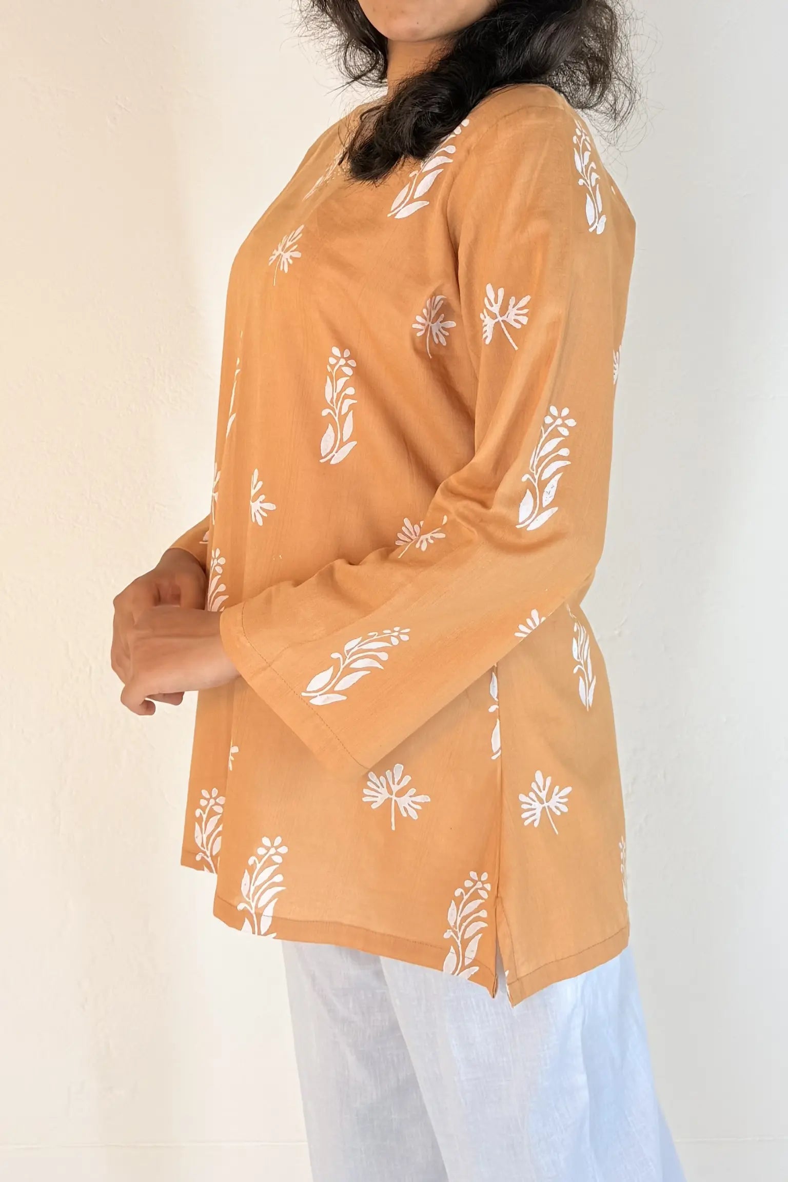 Woman wearing a mustard yellow top with white floral patterns on a plain background