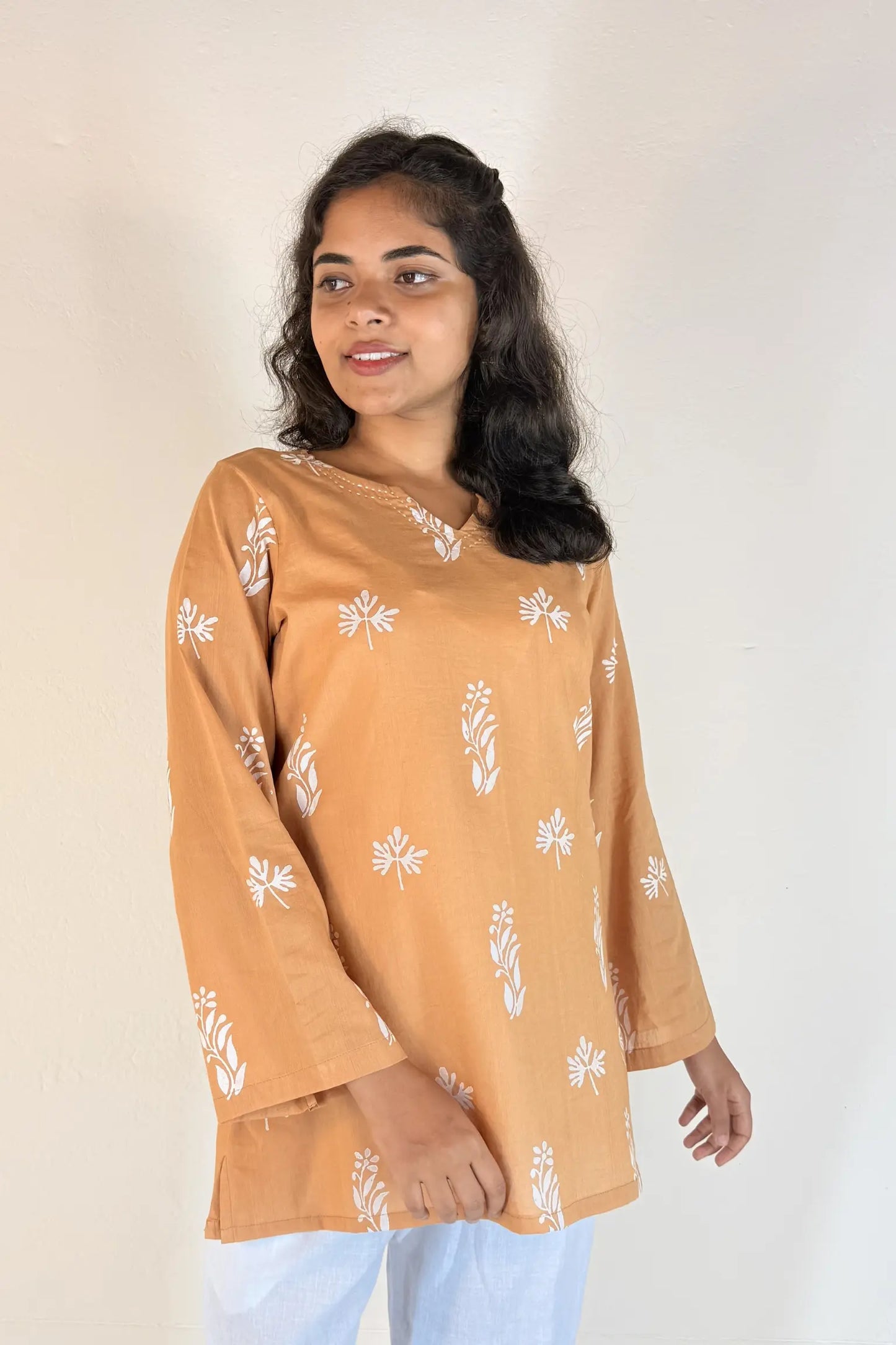 Woman wearing a mustard yellow long-sleeve top with white floral patterns on a plain background