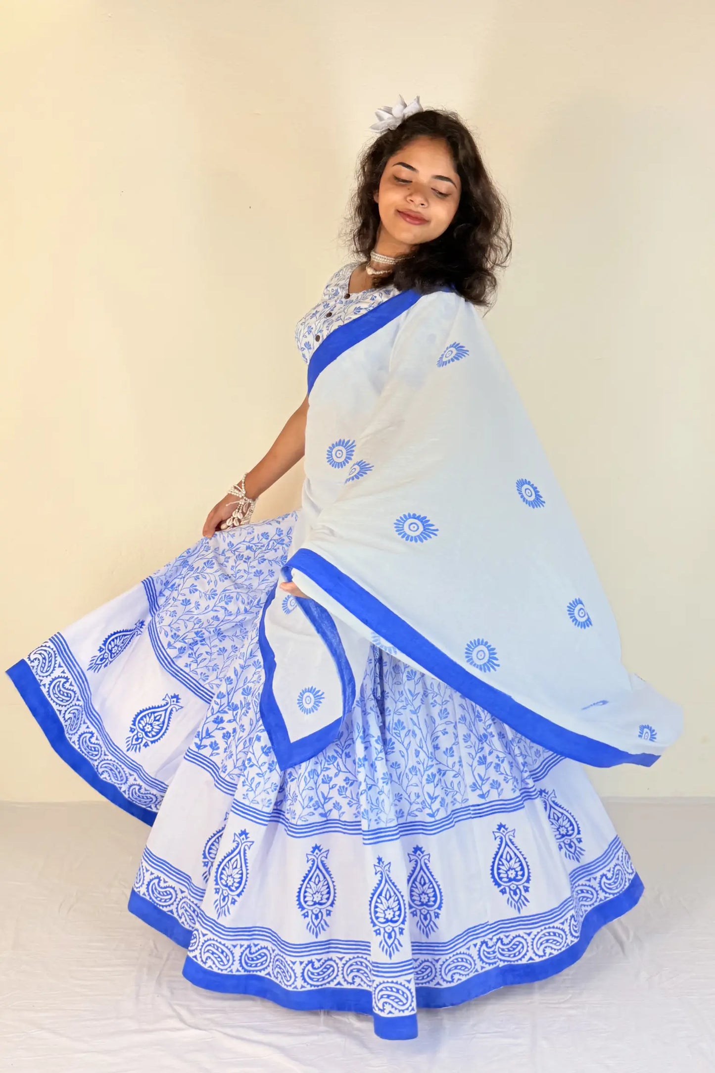 Woman wearing a white Gopi Dress with blue patterns and border on a plain background