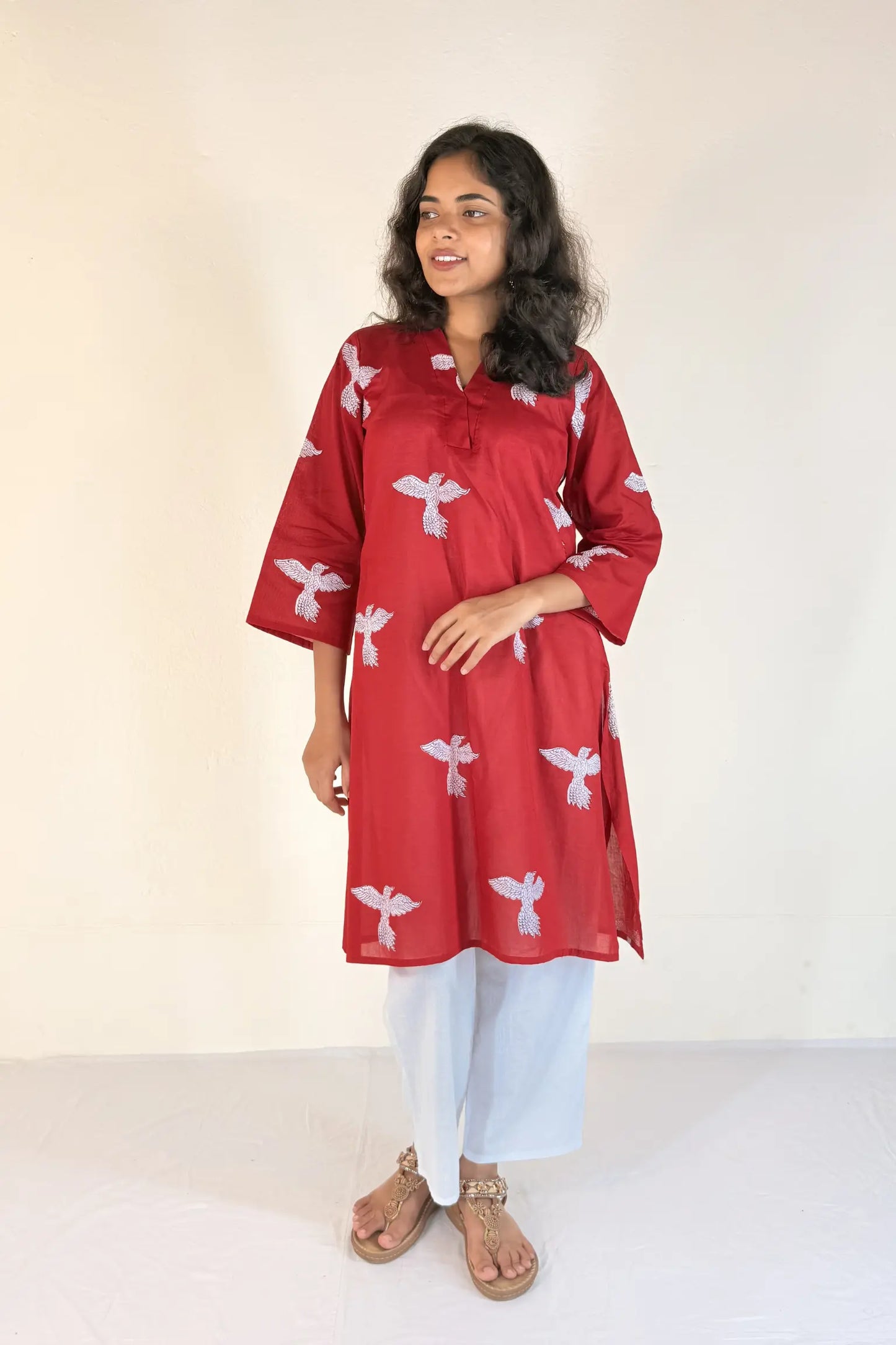Woman wearing a red kurta with white patterns on a plain background