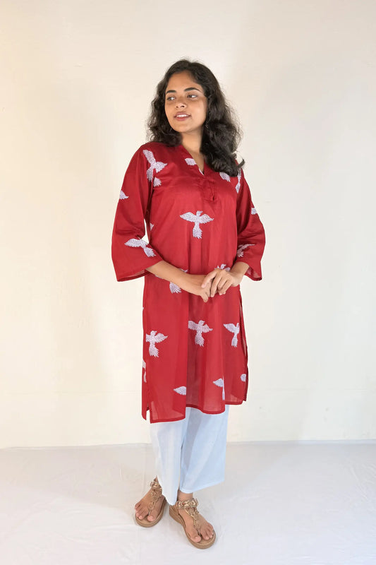 Woman wearing a red kurta with white patterns on a plain background