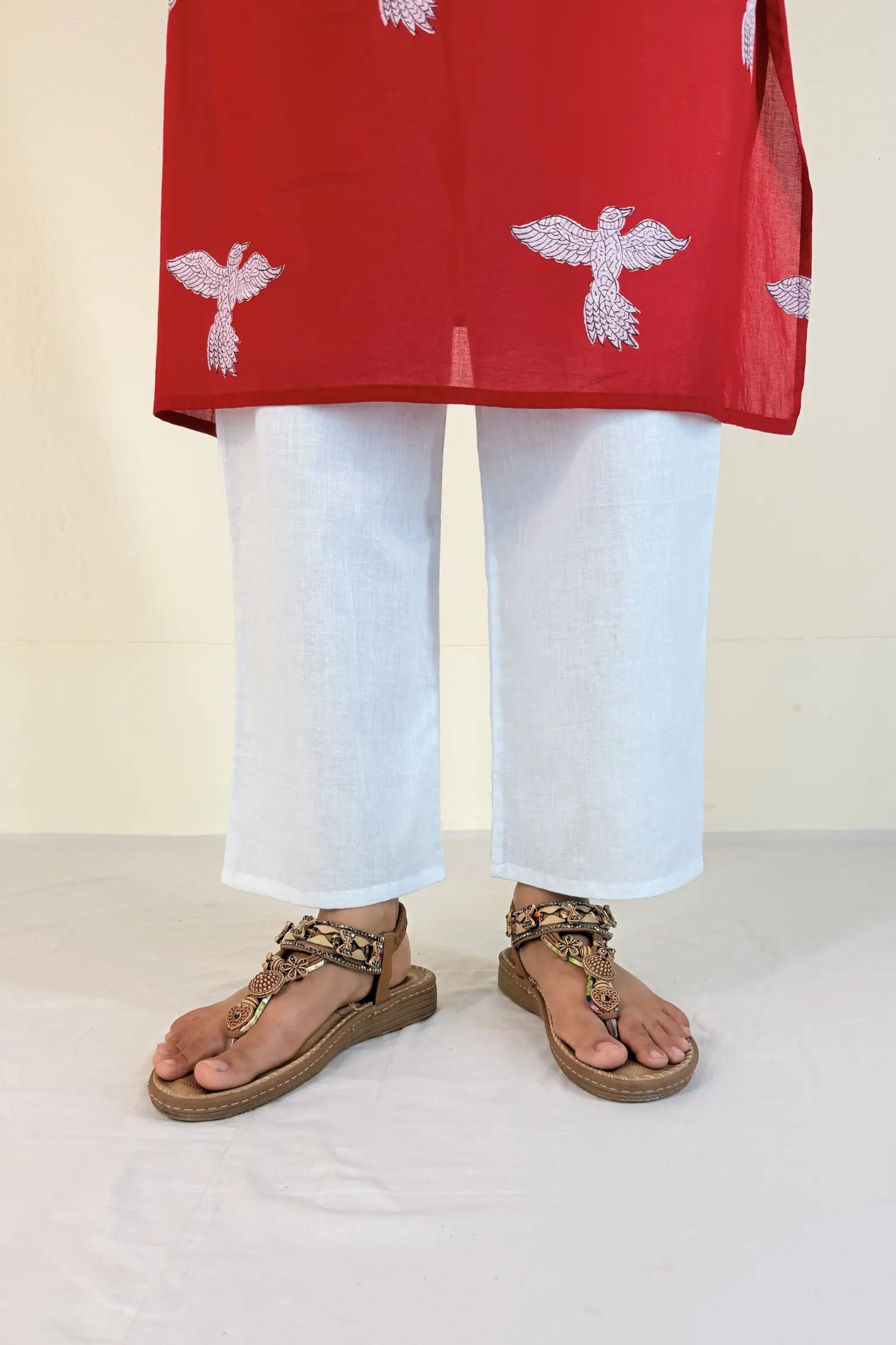 Person wearing a red top with white patterns and white pants on a light background