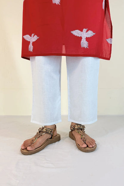 Person wearing a red top with white patterns and white pants on a light background