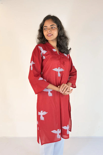 Woman wearing a red kurta with white patterns against a plain background
