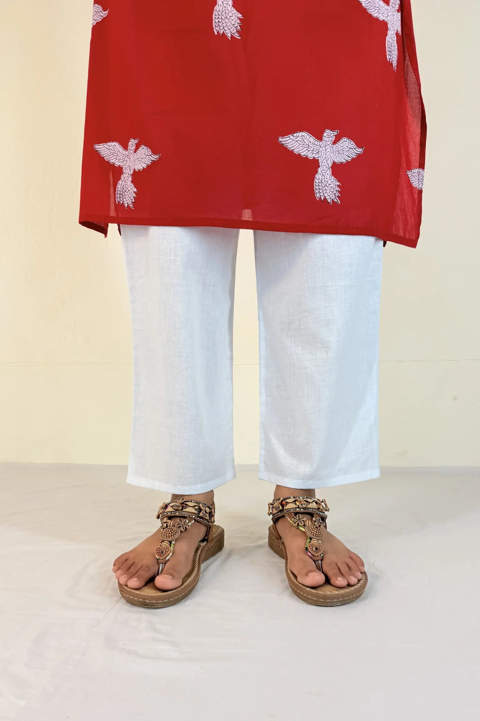 Person wearing a red top with white patterns and white pants, standing on a light-colored floor.