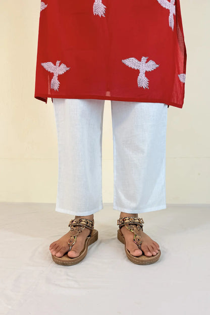 Person wearing a red top with white patterns and white pants, standing on a light-colored floor.