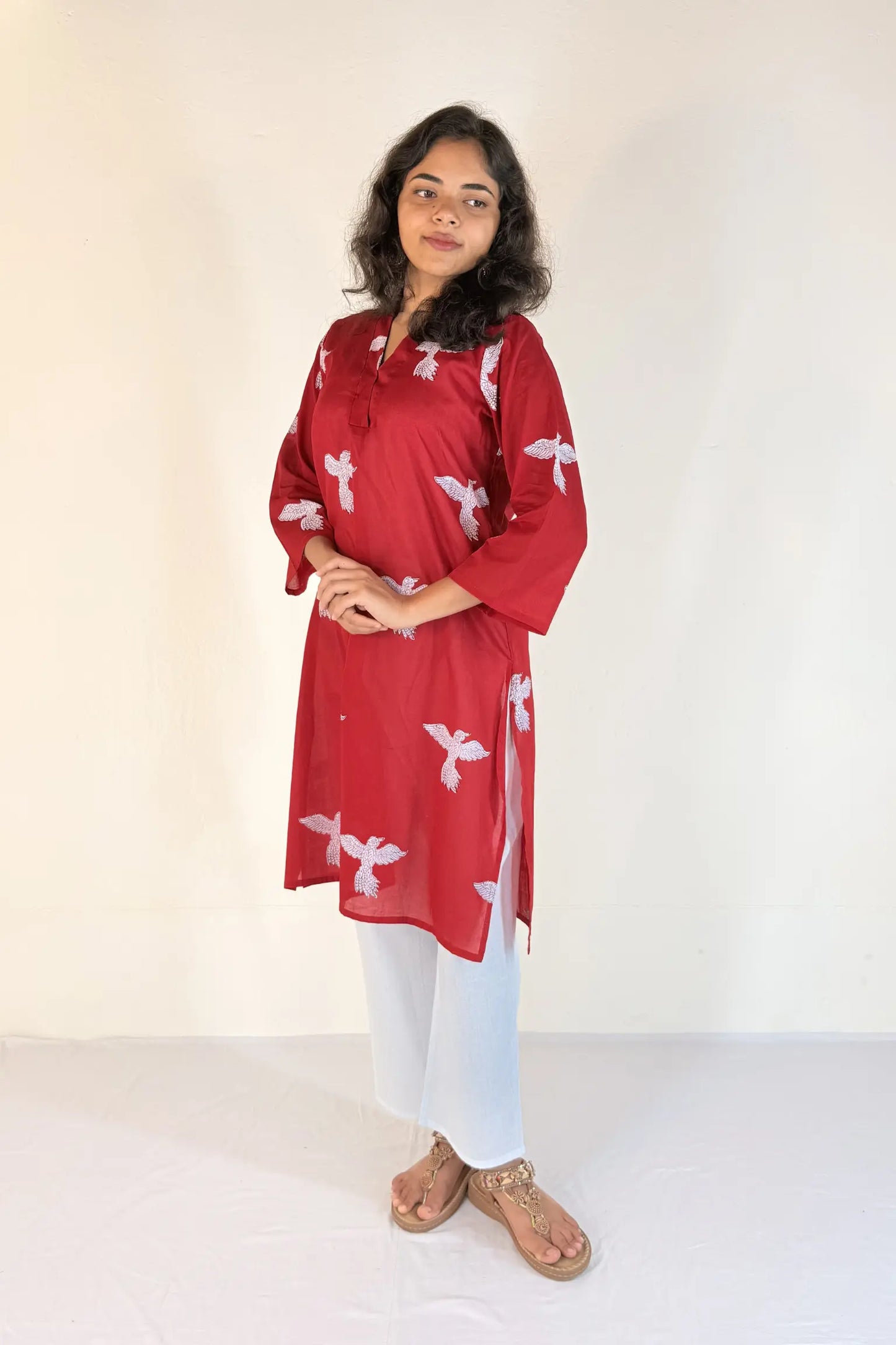 Woman wearing a red kurta with white patterns on a plain background