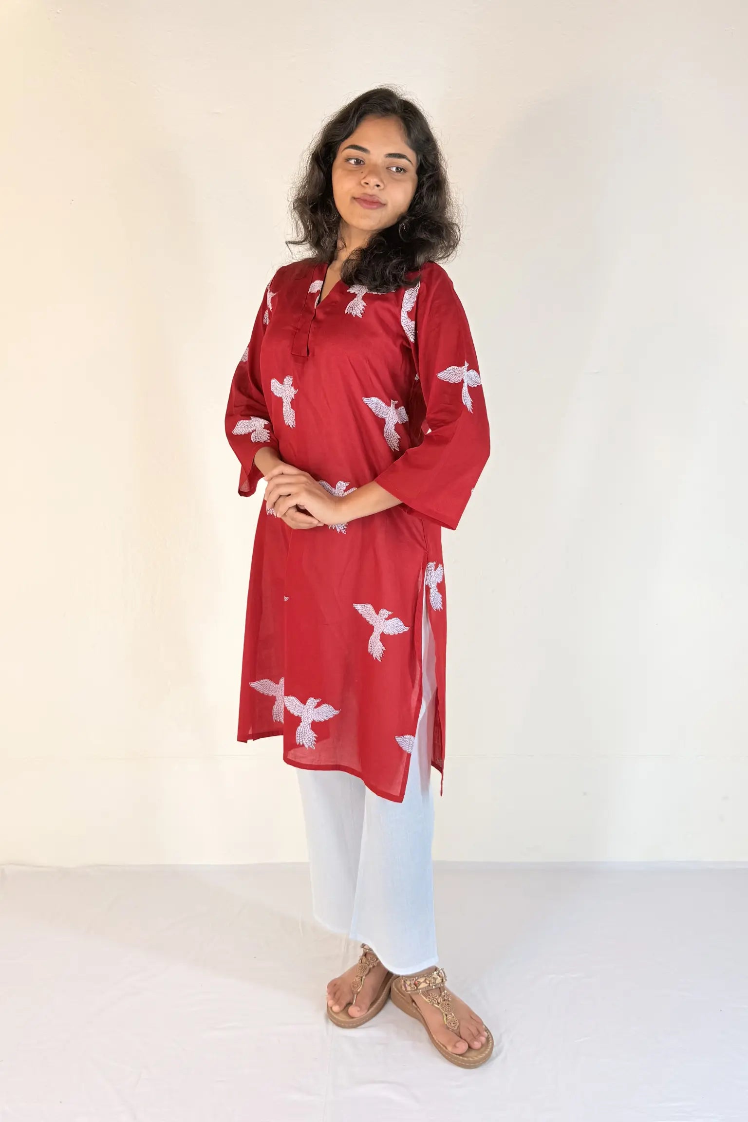 Woman wearing a red kurta with white patterns on a plain background